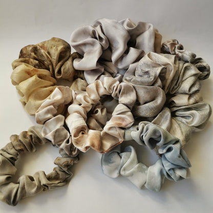 Une collection de chouchous artisanaux en tissu upcyclé aux teintes douces de gris, crème et jaune moutarde, disposés en pile sur un fond blanc neutre.