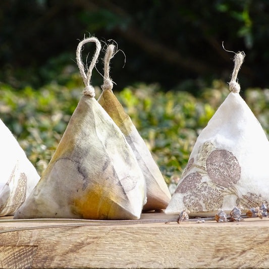 Groupe de sachets de lavande en forme de pyramide (berlingots) en coton blanc, ornés d'empreintes végétales artisanales dans des tons ocre, jaune et brun.