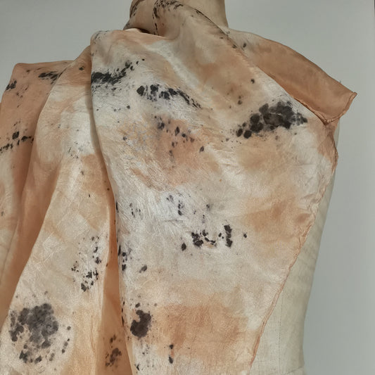 Carré en soie naturelle drapé sur un mannequin, présentant des empreintes botaniques contrastées. Le tissu fluide affiche de larges zones de teinture naturelle saumonées et rosées parsemées de des taches organiques évoquant des taches d'encre sur une soie lumineuse.