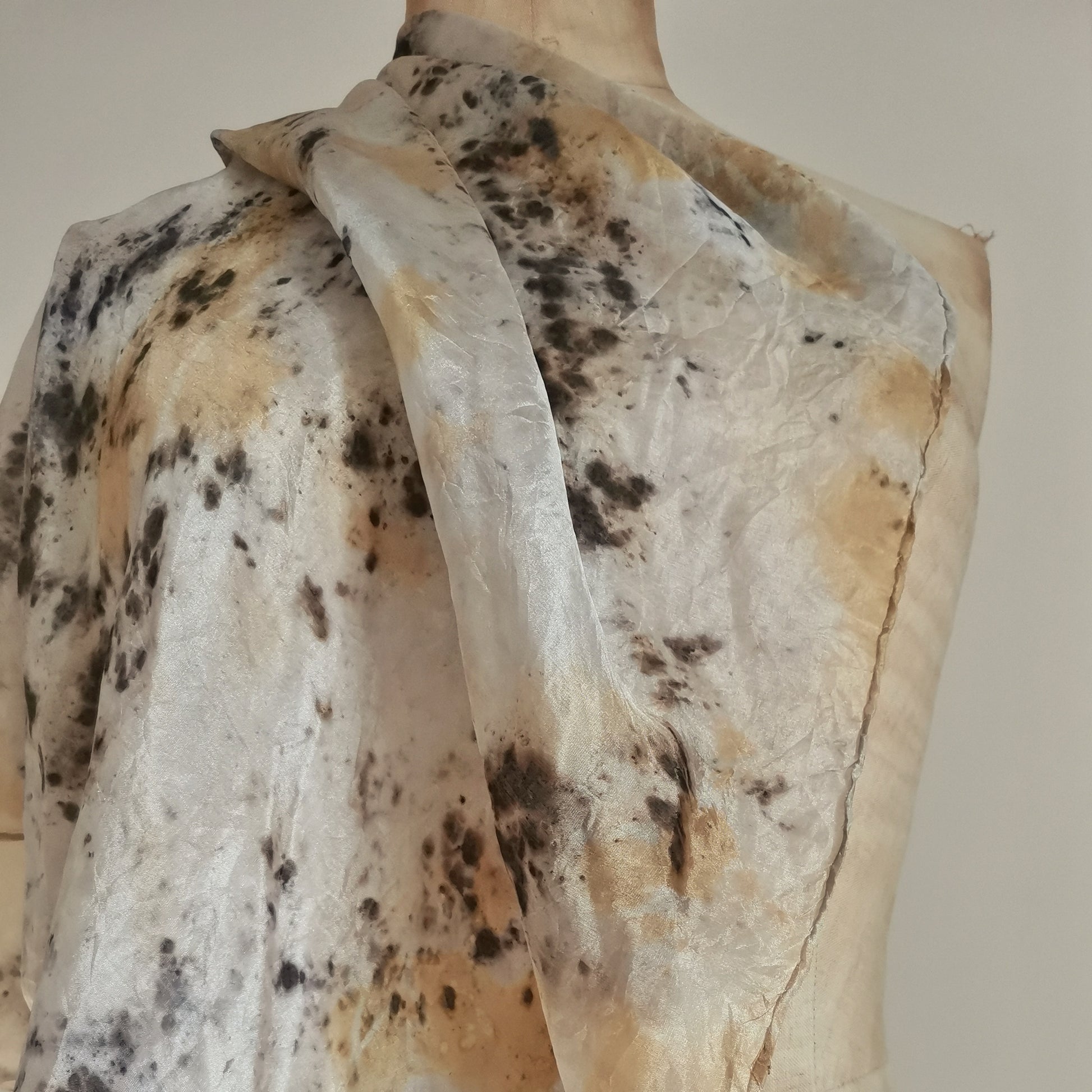 Carré en soie naturelle drapé sur un mannequin, présentant des empreintes botaniques contrastées. Le tissu fluide affiche des taches organiques ocre jaune et des motifs noirs profonds évoquant de l'encre sur une soie lumineuse.