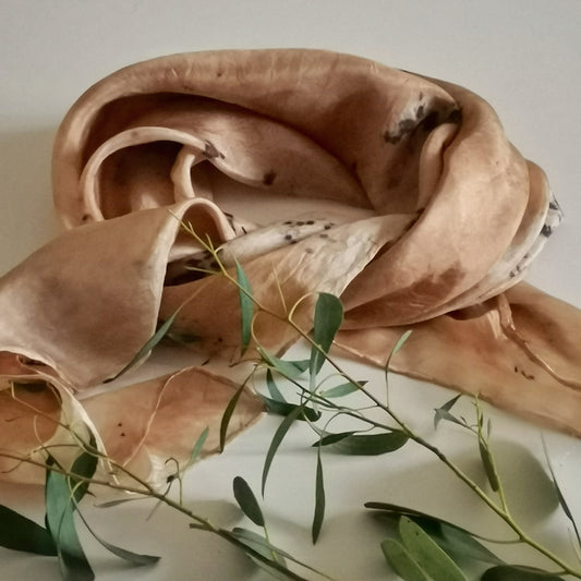 Foulard en soie upcyclée teinté artisanalement aux pigments végétaux, motifs botaniques gris et rose poudré, posé avec une branche d'eucalyptus sur fond clair.