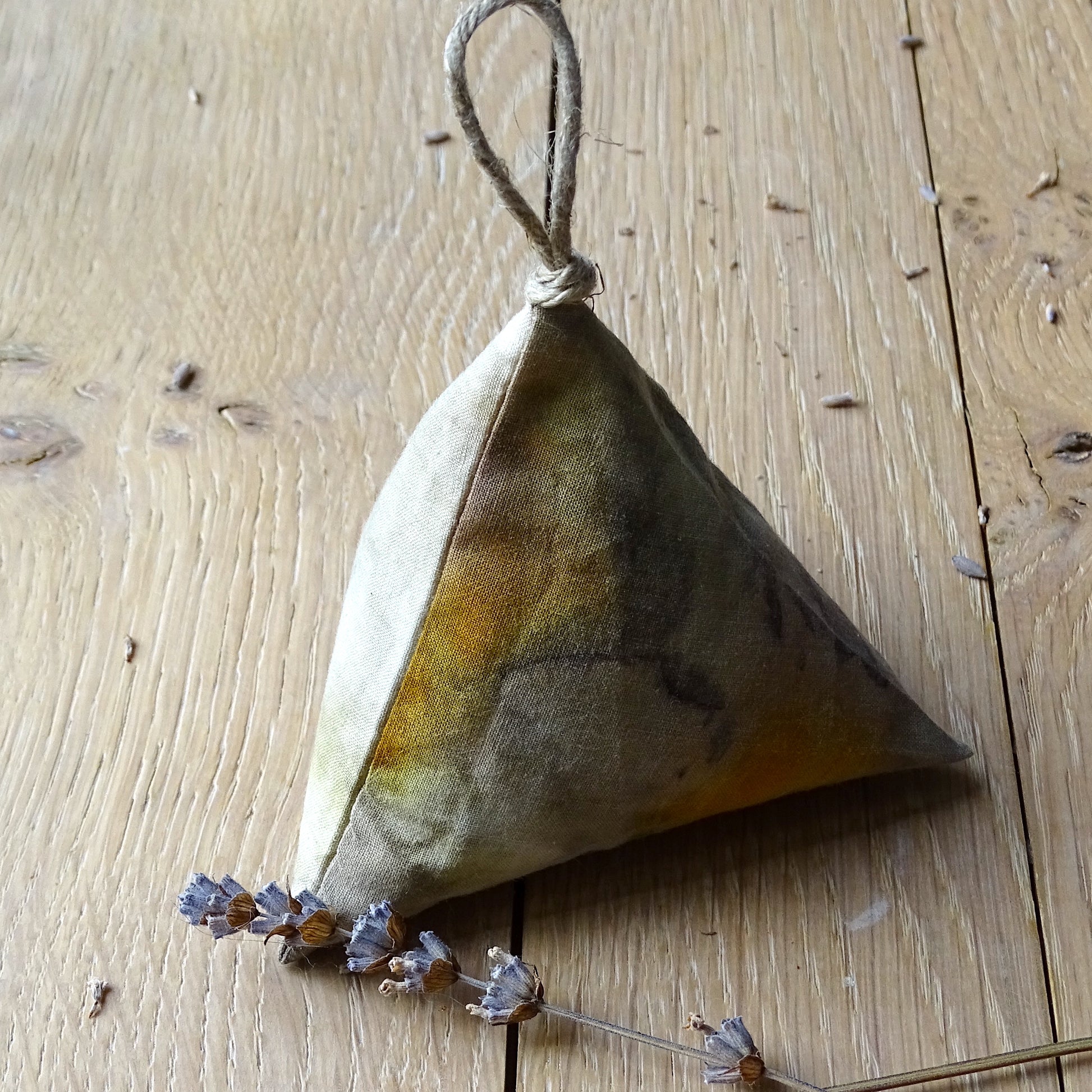 Zoom sur un sachet de lavande berlingot empreintes végétales artisanales dans des tons ocre, jaune et brun, posé sur un bois clair avec des brins de lavande séchée.