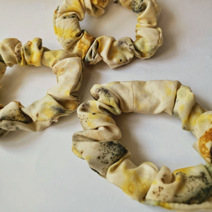 Vue rapprochée de trois chouchous faits main en tissu naturel jaune clair avec des empreintes végétales foncées, mettant en avant la texture du textile et les détails de l'impression artisanale.