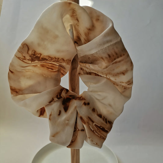Accessoire cheveux en soie teinté à la main suspendu sur un support en bois, révélant des motifs botaniques et minéraux.