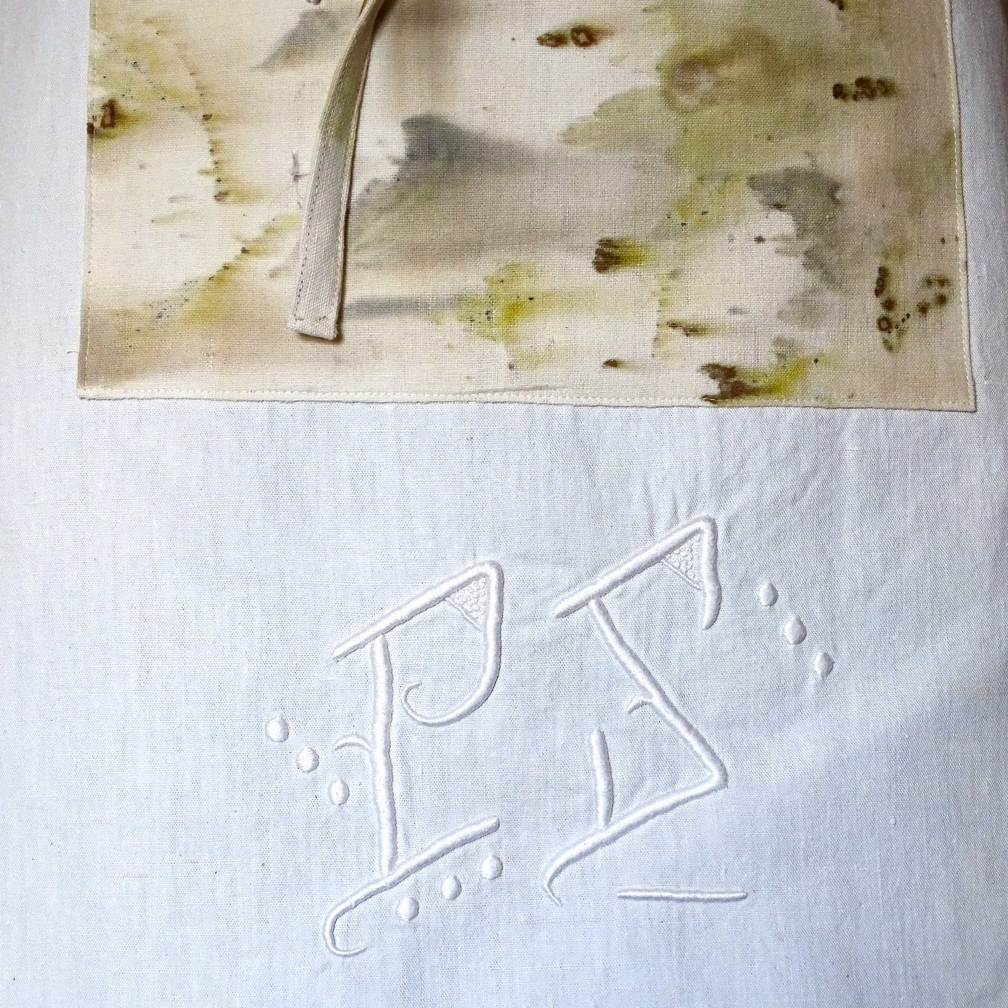 Gros plan sur un monogramme PS brodé à la main sur un drap de trousseau ancien transformé en tablier.